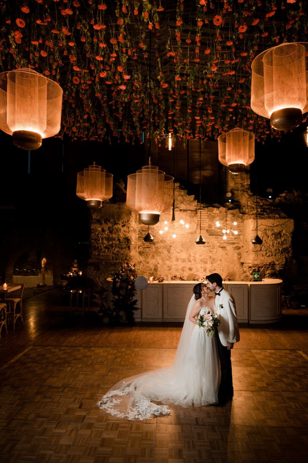 Wide reception shot of the couple kissing under a suspended carnation ceiling by Addy Florales and woven lanterns.