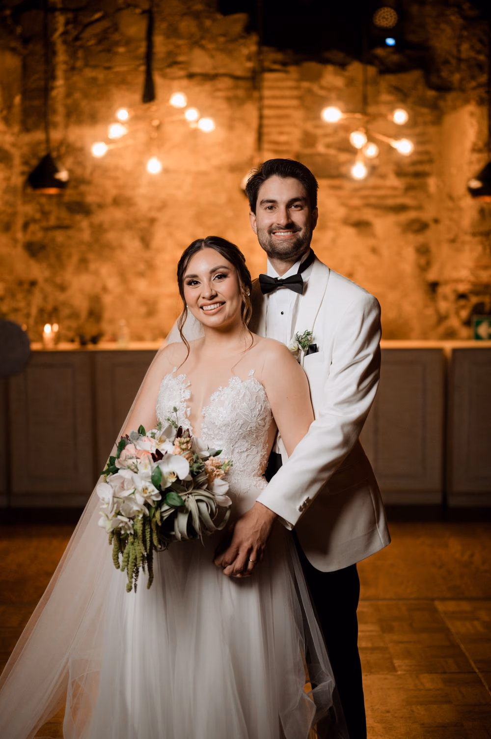Newlywed portrait inside the candle-lit reception with bouquet held forward at Hotel Casa Santo Domingo.