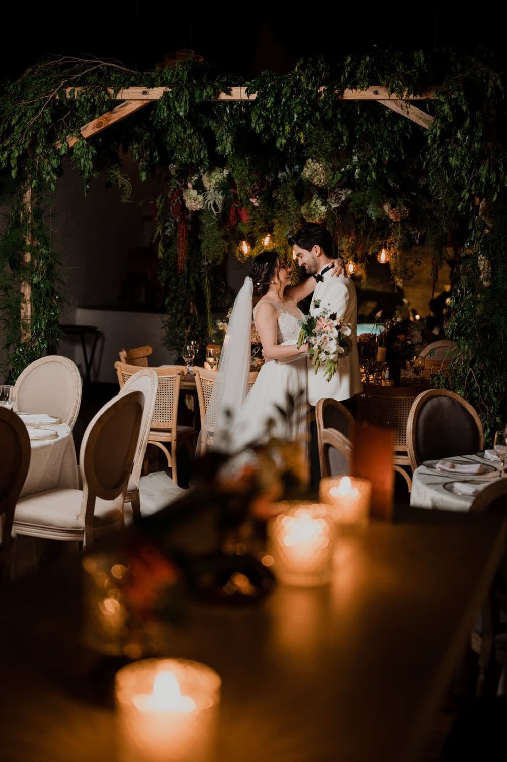 Couple beneath the floral arch dance area framed by lit candles and cane chairs at the colonial monastery reception.