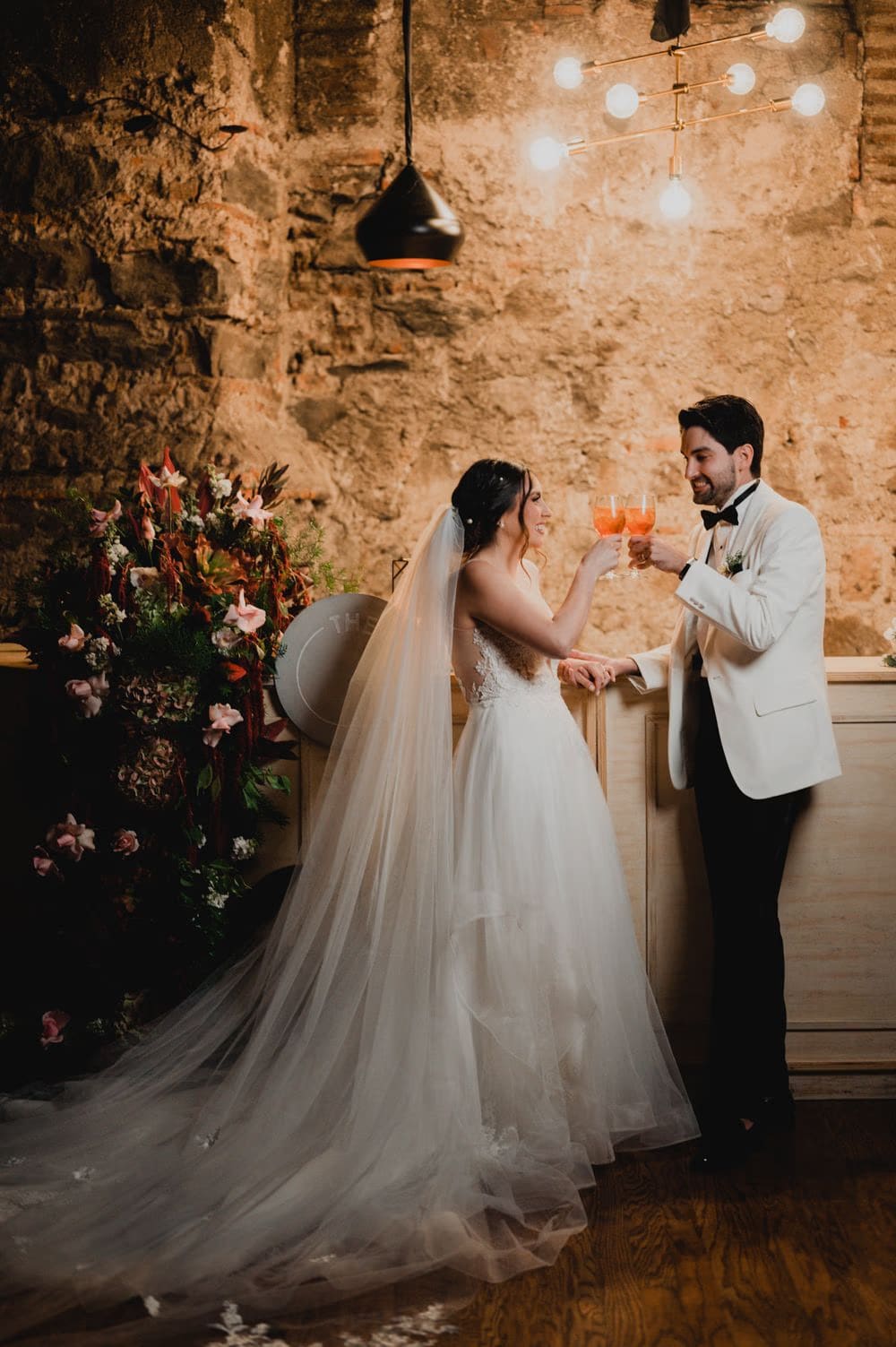 Bride and groom toast aperitivos at the reception bar beside a tall floral arrangement at Casa Santo Domingo.