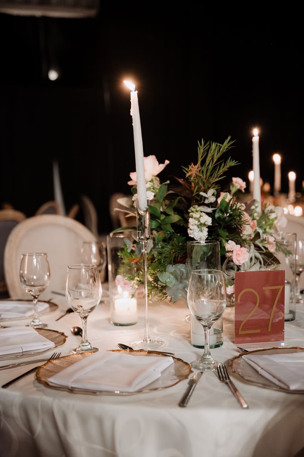 Candle-lit reception table 27 with taper candles and a low arrangement of pink florals and rosemary.