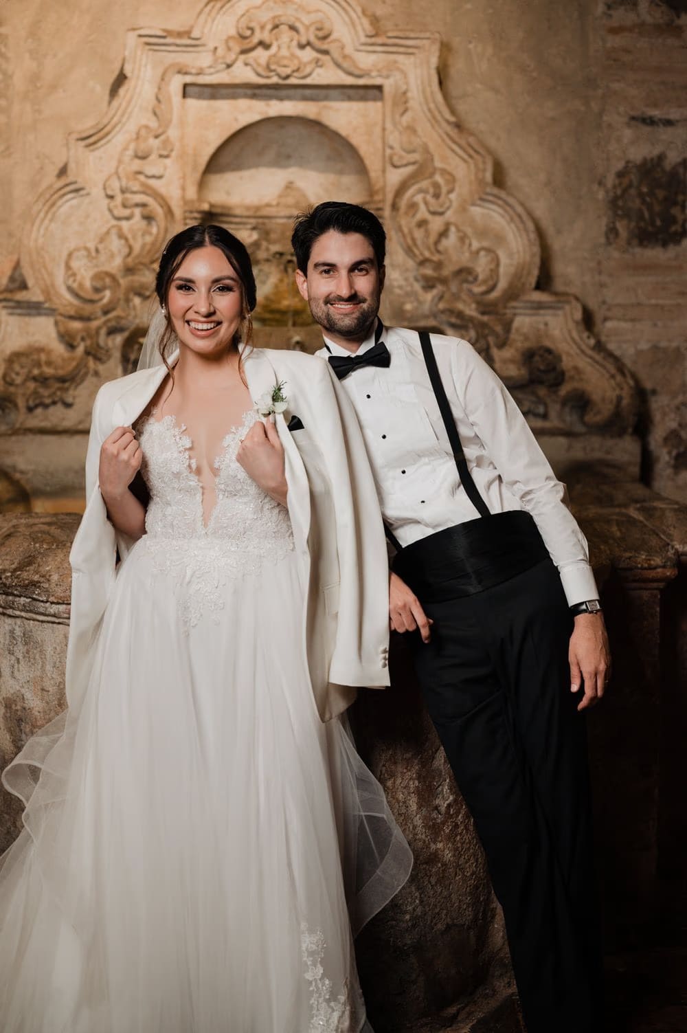 Bride and groom pose in front of an ornate stone fountain niche during portraits at Hotel Casa Santo Domingo.