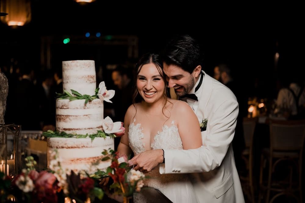 Bride and groom cut a three-tier semi-naked cake with sugar magnolias and amaranth during the reception.