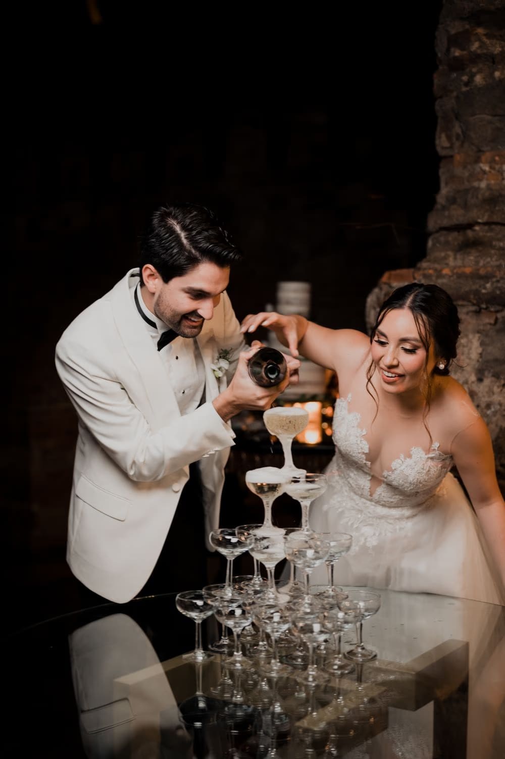 Couple pour the bubbling champagne tower together against an exposed stone wall at Hotel Casa Santo Domingo.