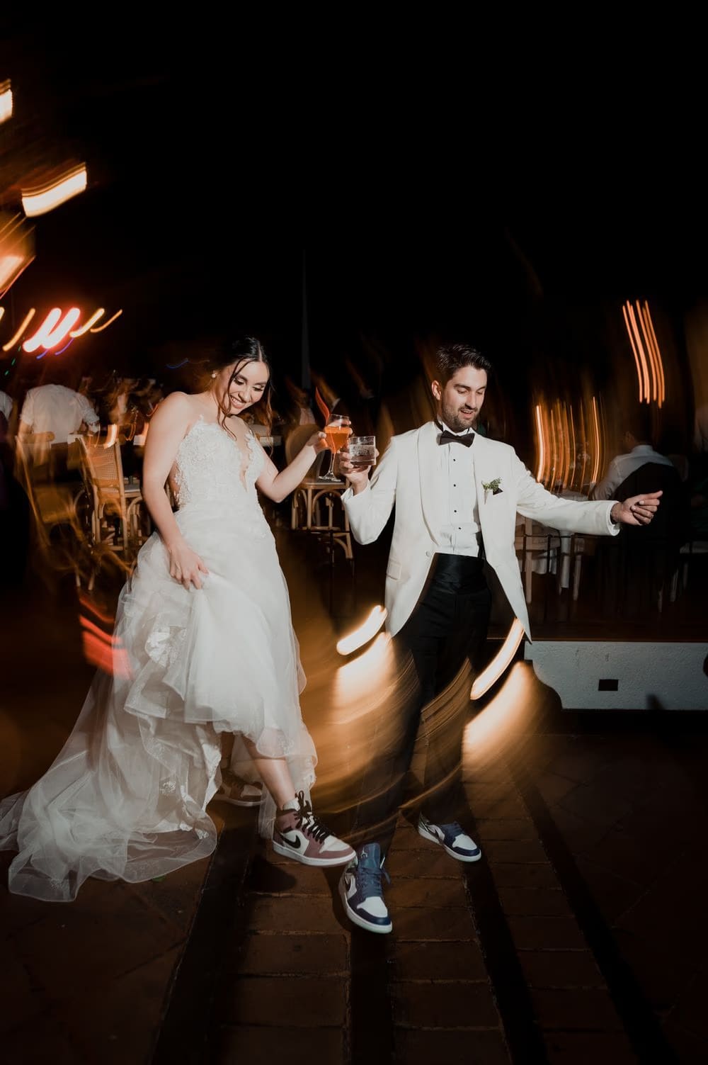 Newlyweds in sneakers dance with cocktails amid streaking light trails during a wild reception moment in Antigua Guatemala.