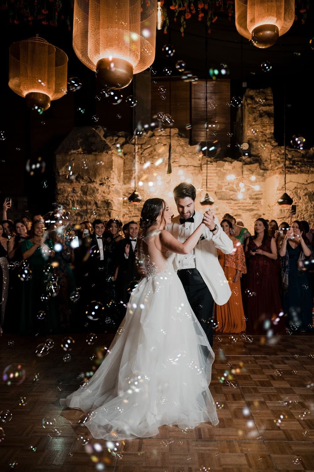 Vera and Ernesto share their first dance beneath glowing woven lanterns and a bubble shower as guests circle the dance floor at Hotel Casa Santo Domingo, Antigua Guatemala.
